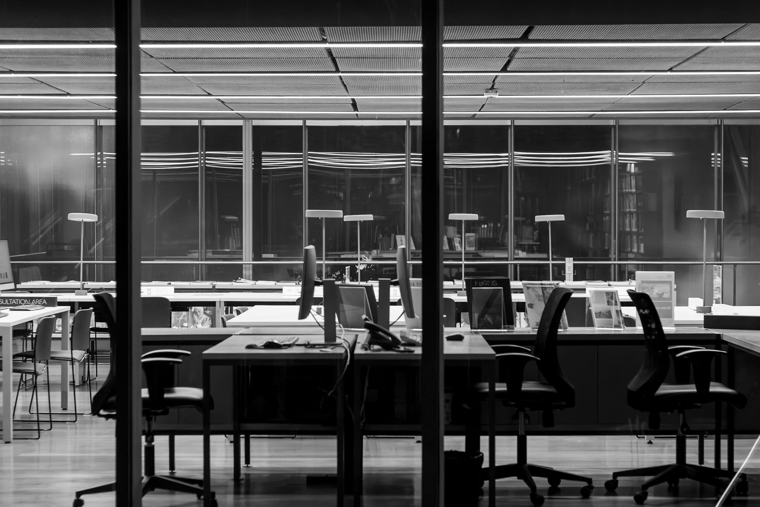 Black-and-white view of a modern commercial office with glass walls, workstations, and task lighting